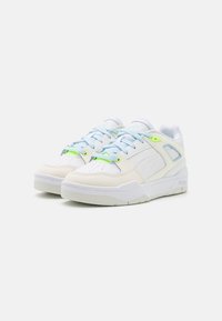 Hvite sneakers med lyseblå snører, lærmateriale, teksturerte detaljer, neongrønne elementer, og et tykt såledesign.
