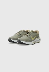 Sport shoes with a lightweight, breathable green mesh upper, beige accents, a yellow swoosh logo, and textured black rubber outsole.