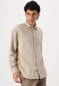 Camisa beige de botones con un sutil patrón de rayas y un solo bolsillo en el pecho, hecha de una tela texturizada. Mangas largas, corte recto.