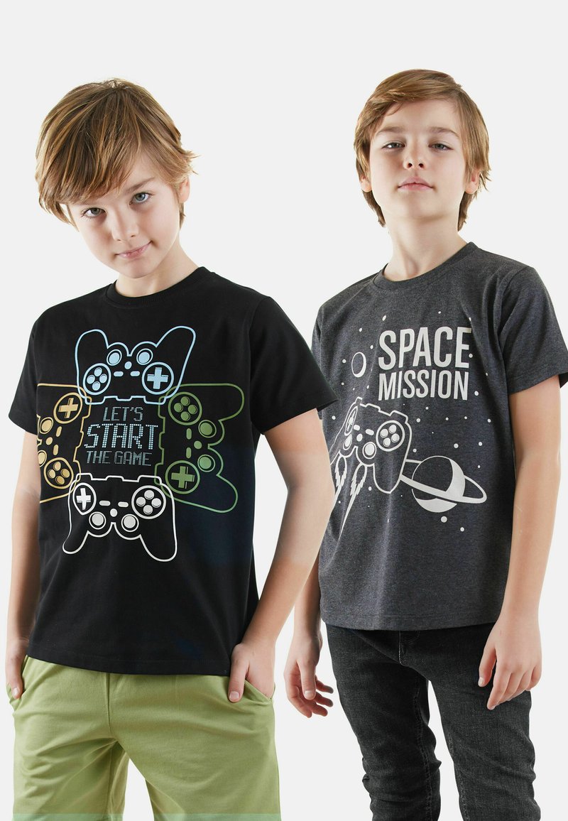 Zwei Jungen tragen bedruckte T-Shirts. Eines ist schwarz mit bunten Spielcontrollern und Text; das andere ist dunkelgrau mit einem Raketen- und Planetendesign.