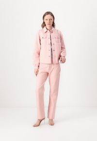 Light pink denim jacket with a button front, two chest pockets, and matching light pink pants, paired with nude heeled sandals.