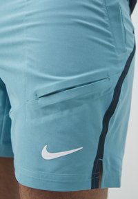 Bermudas deportivas de color azul claro con un bolsillo con cremallera lateral, una franja negra en el costado y el logo de Nike en blanco. Tejido suave y corte ajustado.
