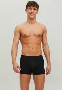 Boxers courts noirs en tissu doux et extensible. Ils offrent une coupe ajustée, une taille élastique et aucune couture visible pour un aspect lisse.