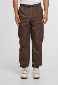 Brązowe spodnie cargo o teksturowanym wykończeniu, z elastycznym pasem, detalem sznurówki i zwężanymi mankietami, w połączeniu z trampkami.