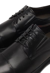 Zwarte lederen dresschoenen met een gladde textuur, traditionele vetersluiting, ronde neus en minimale stiksels langs de bovenzijde.