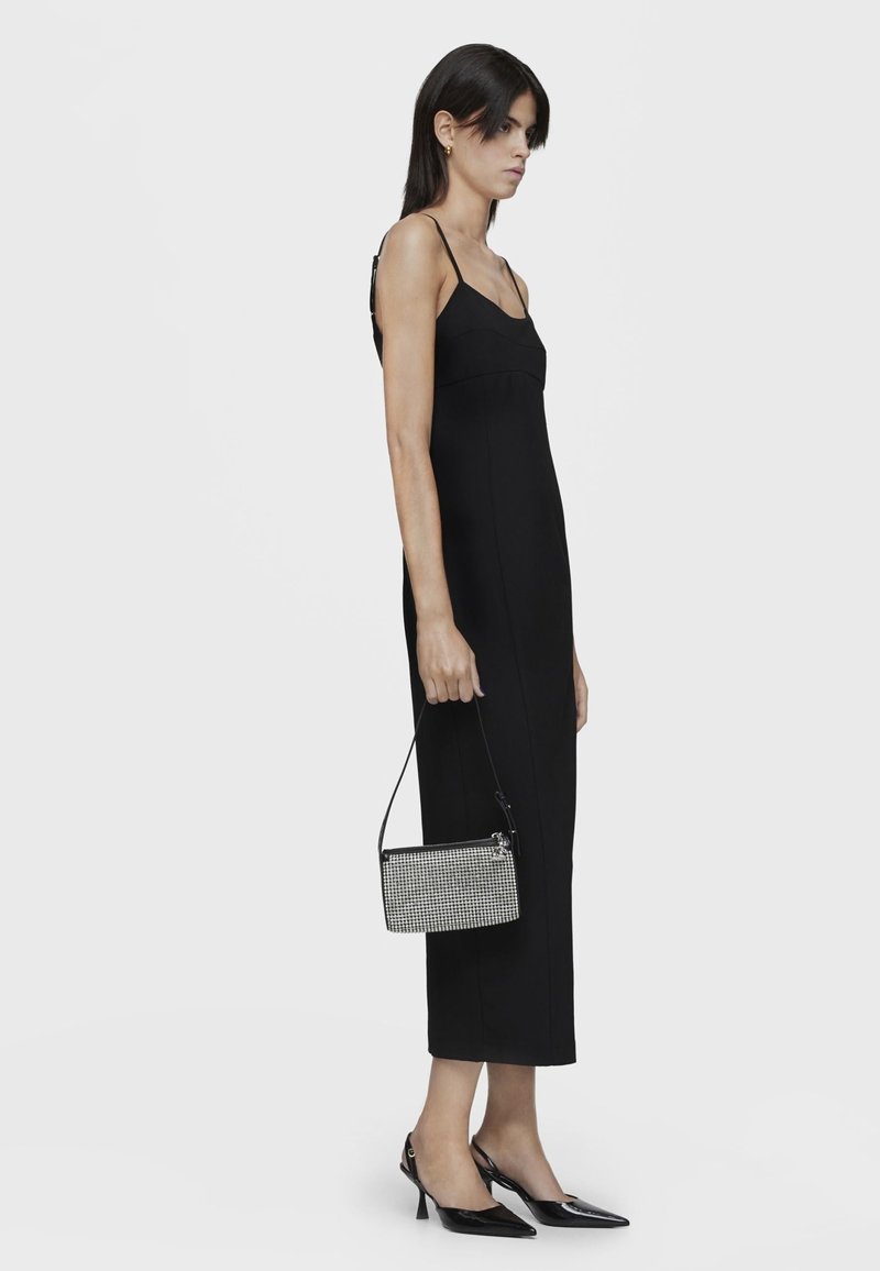 Czarna dopasowana sukienka na cienkich ramiączkach, do długości w połowie łydki. Noszona z ostro zakończonymi czarnymi szpilkami i małą torebką w czarno-białą fakturę.