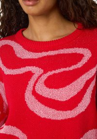 Rdeč pleten pulover z rožnato abstraktno vrtinčasto vzorcem. Tkanina je teksturirana z rebrastim izrezom in ohlapnim prileganjem.
