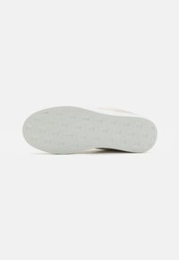 Light gray rubber shoe sole with a textured pattern of squares, featuring embossed logo detail on the heel and smooth edges.