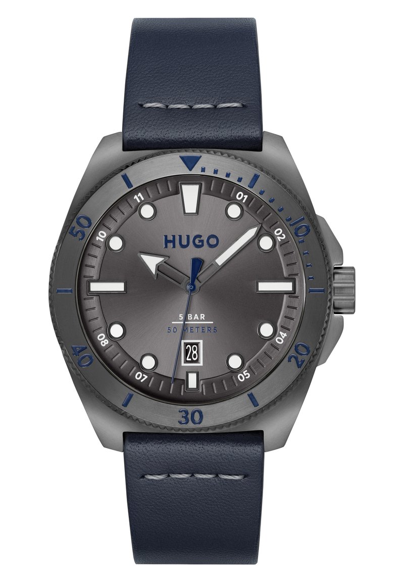 Reloj Hugo con esfera gris, acentos azules y correa de cuero navy. Sus características incluyen marcadores de hora audaces y una ventana de fecha a las 6 en punto.