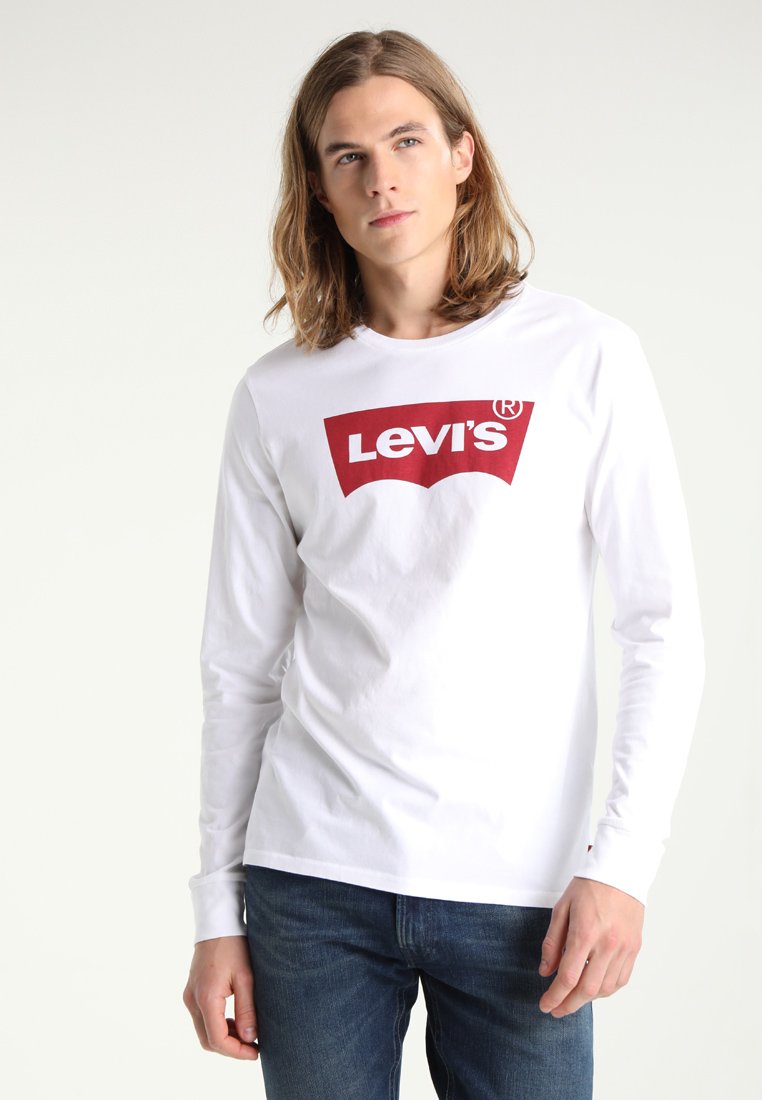 Weißes Langarmshirt mit rotem Levi's-Logo auf der Brust, aus Baumwolle, kombiniert mit blauen Jeans. Schlichte Schnittführung, Rundhalsausschnitt.