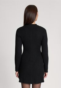 Abito a maglia nero a coste con maniche lunghe, vita aderente e orlo a ruota. Il motivo testurizzato aumenta l'interesse visivo, presentando un colletto rotondo.