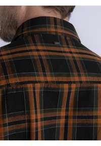 Camisa de cuadros negra con rayas naranjas y verdes, un collar recto y una etiqueta de logo minimalista en la parte posterior cerca del cuello.