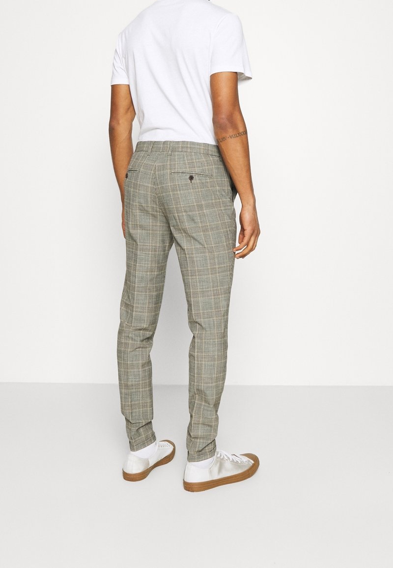 Grijze geruite broek met een slim fit, voorzien van achterzakken en bruine knoopaccenten, gecombineerd met witte sneakers en een wit t-shirt.