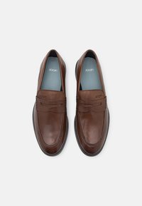 Mocassins en cuir marron légèrement brillants, avec un motif cousu et une semelle en caoutchouc plate. À l'intérieur se trouve une semelle intérieure bleu clair avec le logo de la marque.