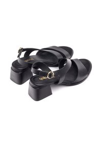 Sandalias de cuero negro con correas estrechas, punta redondeada y tacón grueso. Presentan un detalle de hebilla metálica en la correa del tobillo.