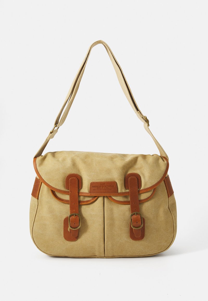 Beige canvas schoudertas met bruine leren accenten, afgeronde klep, twee voorkliksluitingen en een verstelbare schouderband.