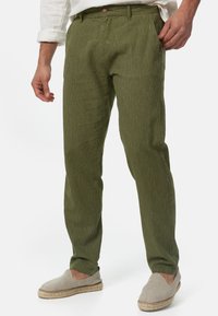 Spodnie w oliwkowo-zielone paski z lekkiego materiału, charakteryzujące się klasycznym krojem, bocznymi kieszeniami i zapięciem na guziki. Połączone z jasnoszarym obuwiem.