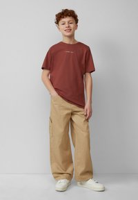 Bruine katoenen T-shirt met korte mouwen, gecombineerd met beige cargobroek met zijzakken en afgewerkt met witte sneakers.
