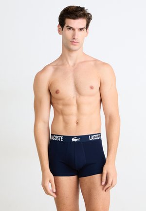 Boxer-briefs bleu marine en tissu doux, dotés d'une ceinture élastique blanche avec le logo "LACOSTE" et l'emblématique crocodile.