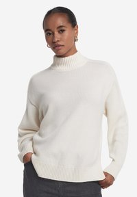 Cremefarbener Strickpullover mit hohem Rippenkragen, weiter Passform und gerippten Säumen. Weiche Textur, lange Ärmel und minimalistische Designdetails.