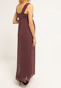 Lång, ärmlös klänning i burgundrofärg gjord av genomskinligt tyg, med breda axelband och en figurnära överdel, som flödar ner till golvet med en lätt glans.