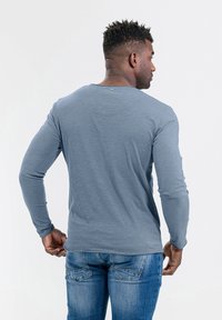 Lange mouwen, lichtblauw shirt met een ronde halslijn en geribbelde manchetten, gecombineerd met blauwe spijkerbroek. Gelaagde stof met een subtiel heatherpatroon.