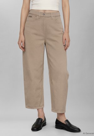 Béžové nohavice s vysokým pásom a rovnými nohavicami, skrátené nad členky, nosené s čiernymi koženými mokasínami a bielym tielkom bez rukávov.