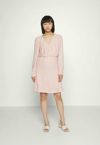 Vestido rosa com um design envelopado, mangas longas e um tecido texturizado. Apresenta um decote em V e uma cintura ajustada, estendendo-se até uma saia rodada.