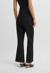 Zwarte flared pants van gladde stof, met een middelhoge taille, een achterzak en gecombineerd met puntige zwarte muiltjes.