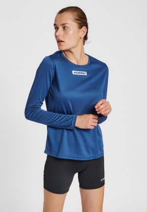 Blauwe sportshirt met lange mouwen van gladde stof, met een ronde halslijn en een wit logolabel op de borst. Zwarte shorts daaronder.
