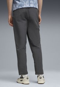 Graue, leichte Hosen mit schlankem Schnitt und Seitentaschen, kombiniert mit hellen Sportschuhen und weißen Socken.