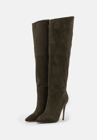 Vysoké olivově zelené semišové boty s špičatými špičkami a jehlovými podpatky. Hladký povrch s minimálními detaily a čistými liniemi.