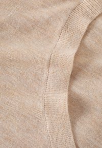 Beige gebreide trui stof met een zachte textuur. Zichtbare ribbelrand en een gladde afwerking, met subtiele kleurvariaties.