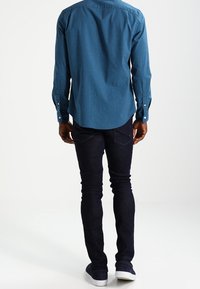 Chemise à carreaux bleue à boutons, manches longues, avec un ourlet incurvé, associée à un jean slim foncé et des chaussures bateaux bleu marine.