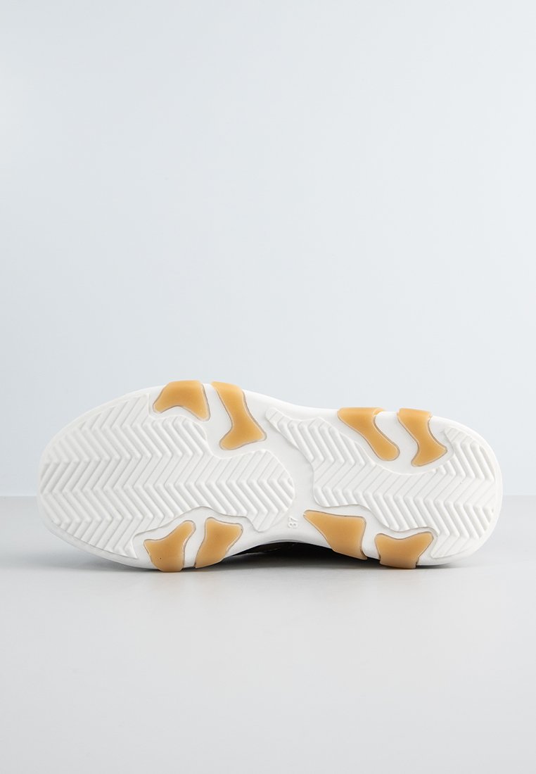 Suola di una sneaker con base bianca, materiale in gomma, motivo a spina di pesce e dettagli arancioni per aderenza e trazione.