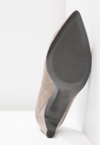 Chaussure à talon aiguille en daim taupe avec un bout pointu, semelle en caoutchouc noir texturé et couture discrète sur le côté. Conçue pour une apparence élégante.