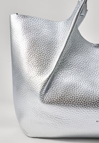Zilveren leren tote bag met een gestructureerd oppervlak, voorzien van een brede opening en een enkele schouderband. Minimalistisch ontwerp zonder zichtbare hardware.