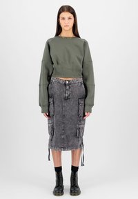 Rövidített olívazöld pulóver kerek nyakkal; szürke farmer midi szoknya cargo zsebekkel; fekete fűzős csizmák.