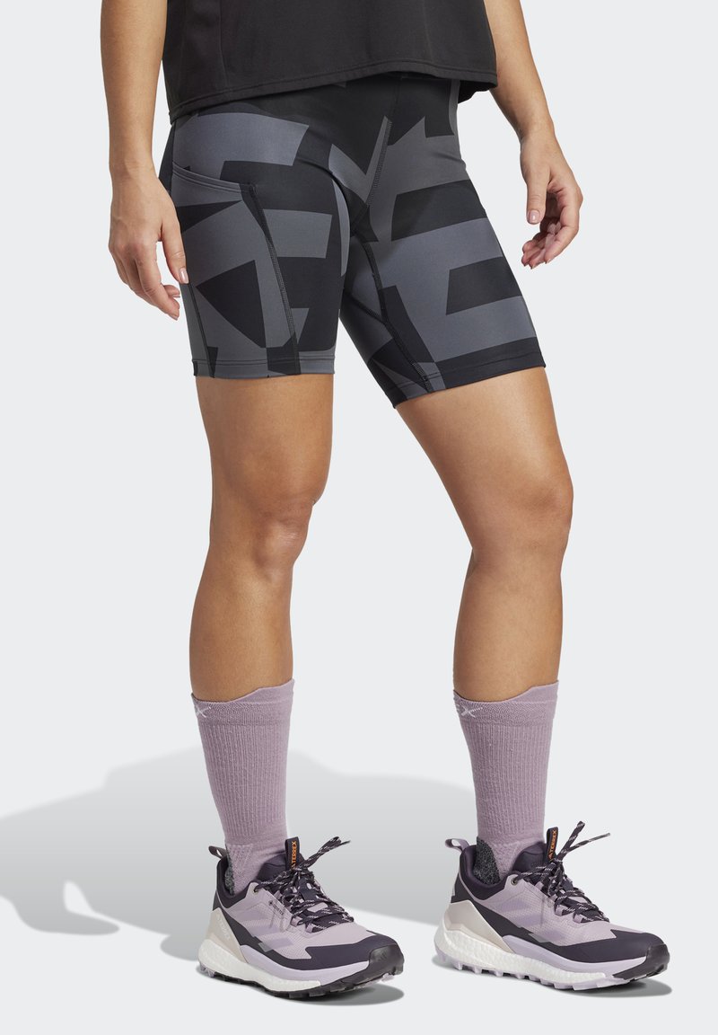 Čierne a šedé šortky s vzorom a priliehavým strihom, doplnené fialovými ponožkami a šedými teniskami s čiernymi akcentmi.