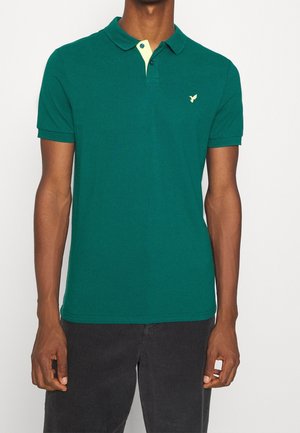 Groen poloshirt met een contrasterende gele kraag, voorzien van een klein logo op de borst, korte mouwen en een klassiek ontwerp.
