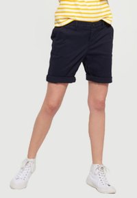 Navy blue shorts made of cotton, featuring a rolled hem and side pockets. Worn with a yellow-striped shirt and white sneakers.