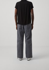 Loose-fitting black short-sleeve shirt with a back yoke, paired with lightweight gray trousers featuring a crinkled texture and side pockets.