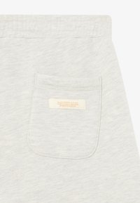 Pantalones de algodón gris claro con un pequeño bolsillo trasero. El bolsillo cuenta con una etiqueta con texto color crema. Tejido suave y texturado.