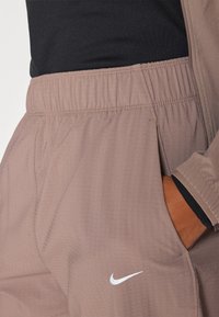 Lichte Nike joggers in een zachte beige stof met een elastische tailleband, zijzakken en een witte logo-accent bij de zoom.