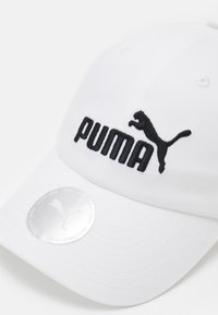 Gorra de béisbol blanca con el logotipo negro bordado de "PUMA" y el gráfico de un puma saltando. Correa ajustable en la parte posterior. Textura suave de algodón.