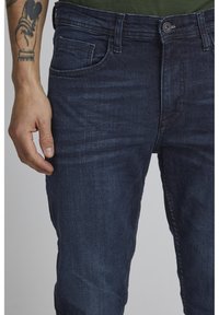 Tummansiniset farkut slim fit -mallissa, joissa on viisi taskua, hienovarainen ommel ja sileä pinta.