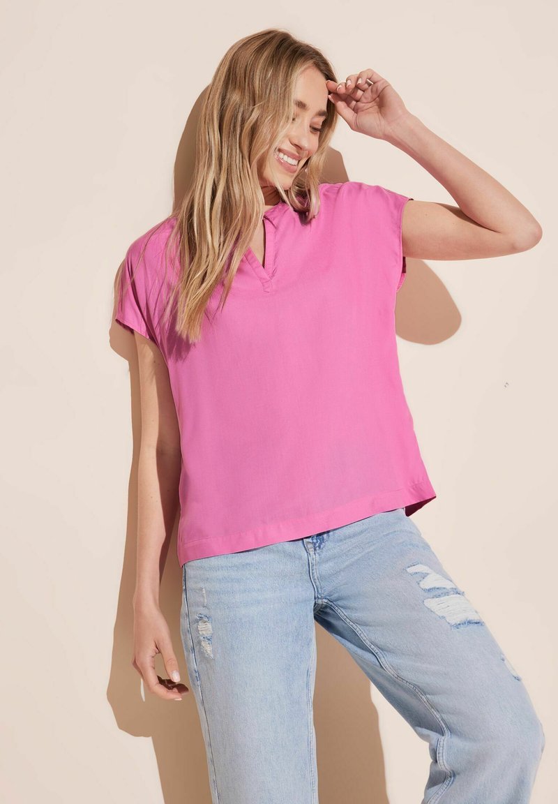 Blusa colletto rosa a maniche corte realizzata in tessuto leggero, abbinata a jeans dritti chiari e strappati.