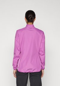 Giacca leggera viola con maniche lunghe, colletto alto e dettagli riflettenti. Presenta tasche laterali con zip, una texture liscia e un branding discreto.