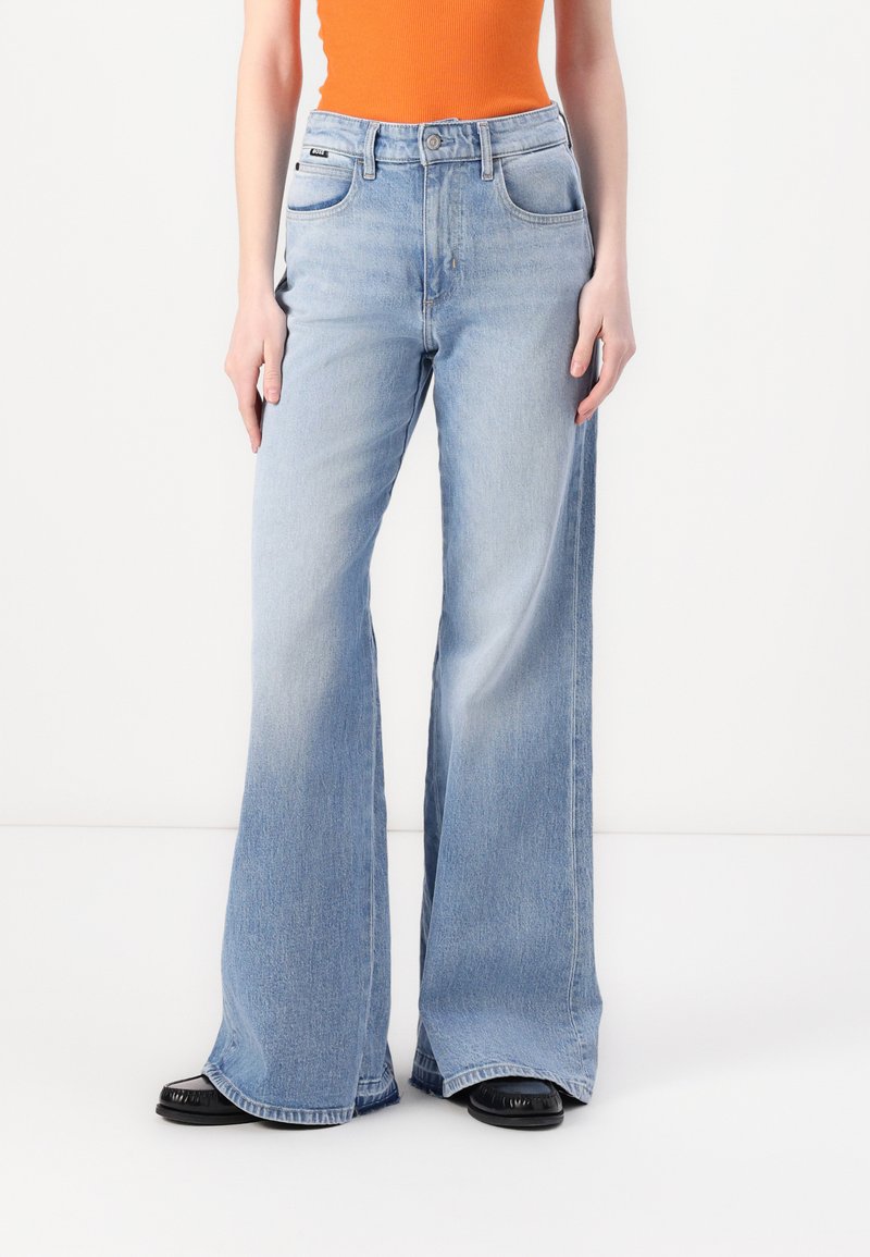 Lyseblå vide jeans med høy midje, fem-lommer design og subtil fading. Materialet ser ut til å være solid denim med en jevn tekstur.