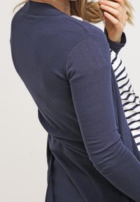 Marinblå långärmad cardigan i mjukt material, med randigt mönster på framsidan. Enkel design med en avslappnad passform.